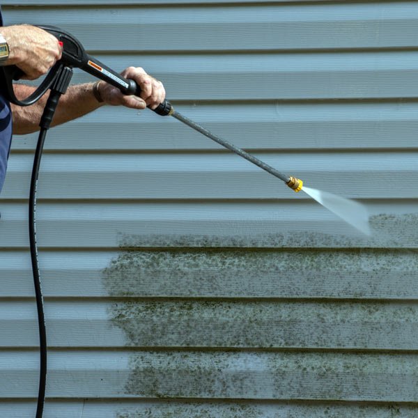 Person uses a pressure washer to clean moldy siding on a house exterior.