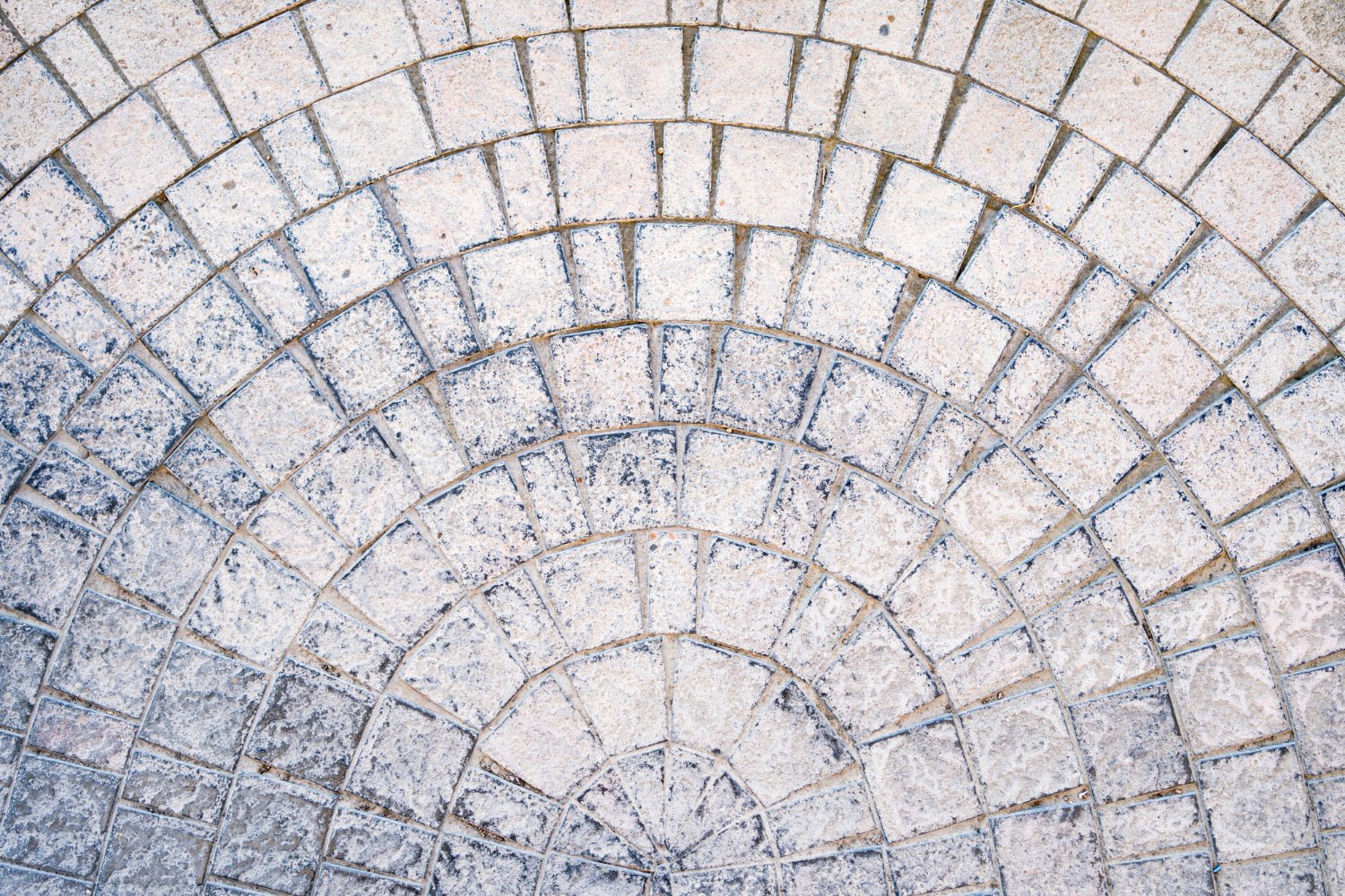 Concentric circular stone pavement made of light gray rectangular pavers forming a stepped pattern on the ground.