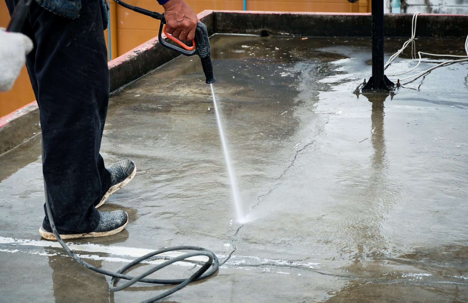 Person using a pressure washer to clean a wet concrete surface, spraying a jet of water onto the floor.