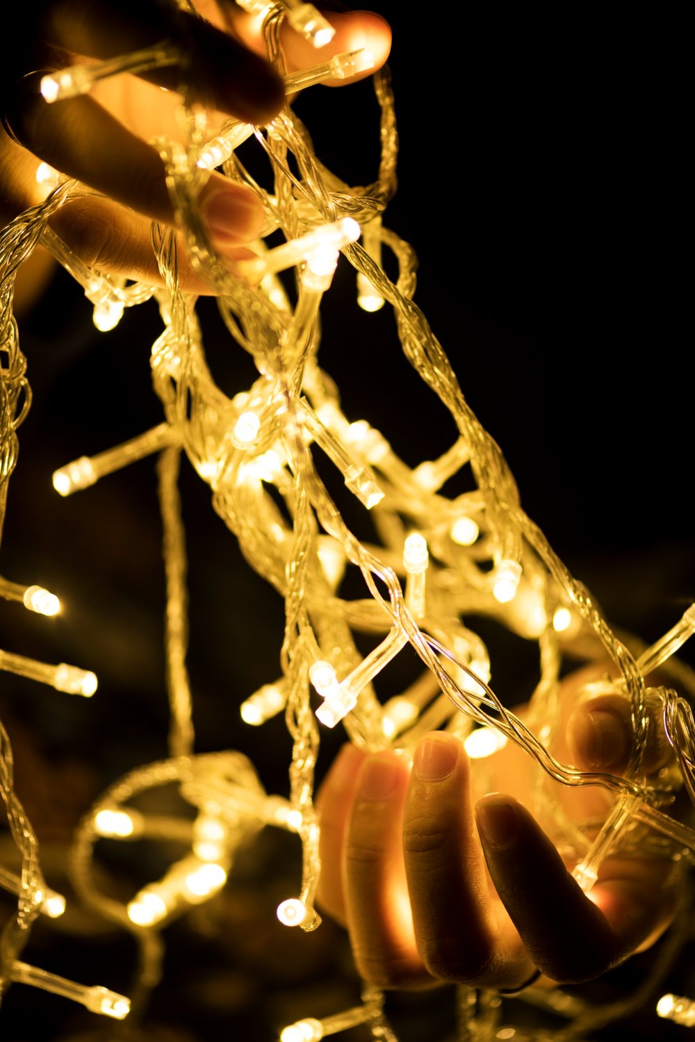 Close-up of fingers weaving warm-white fairy lights against a dark background.