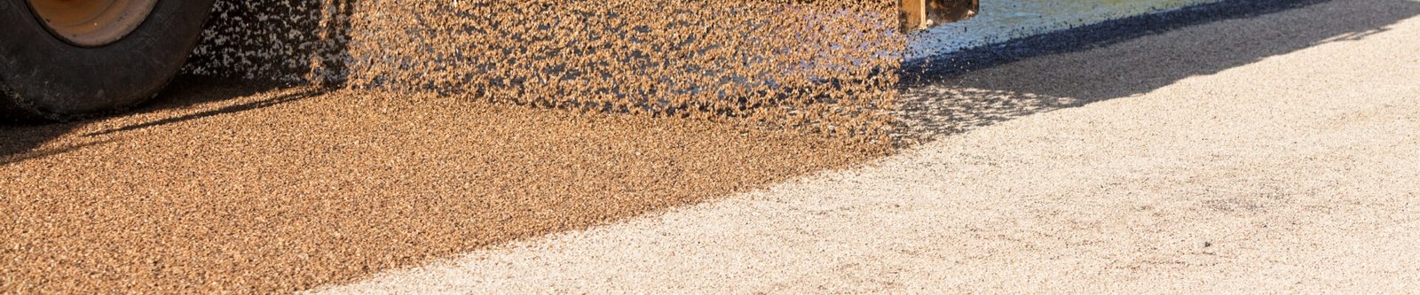 Gravel being dumped from a truck onto an asphalt road, with a tire visible on the left.