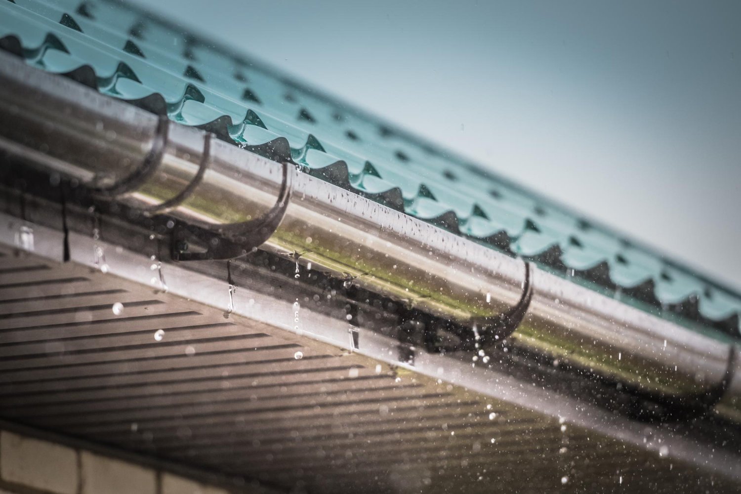 Rain-drenched gutter along a teal tiled roof with raindrops falling nearby