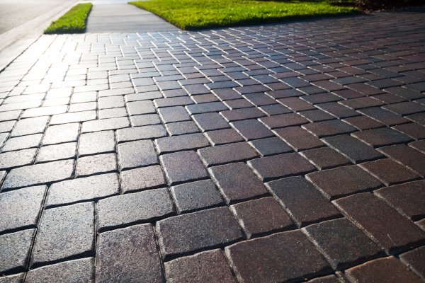 Brick-paved sidewalk and road with green grassy verge on the side, sunlight reflecting off the bricks.