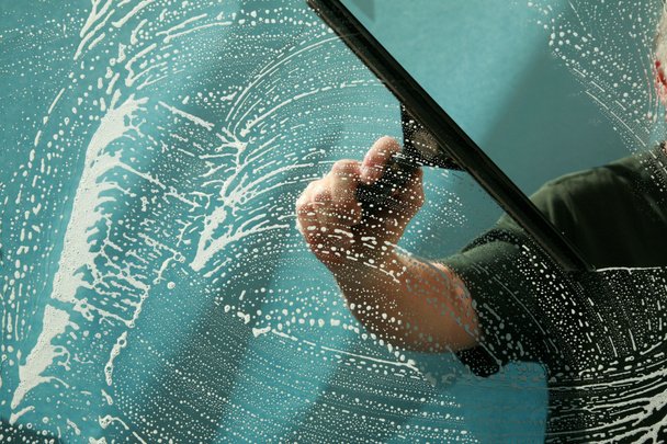 Close-up of a hand holding a squeegee, cleaning a car window with soap bubbles on the glass banishing streaks.