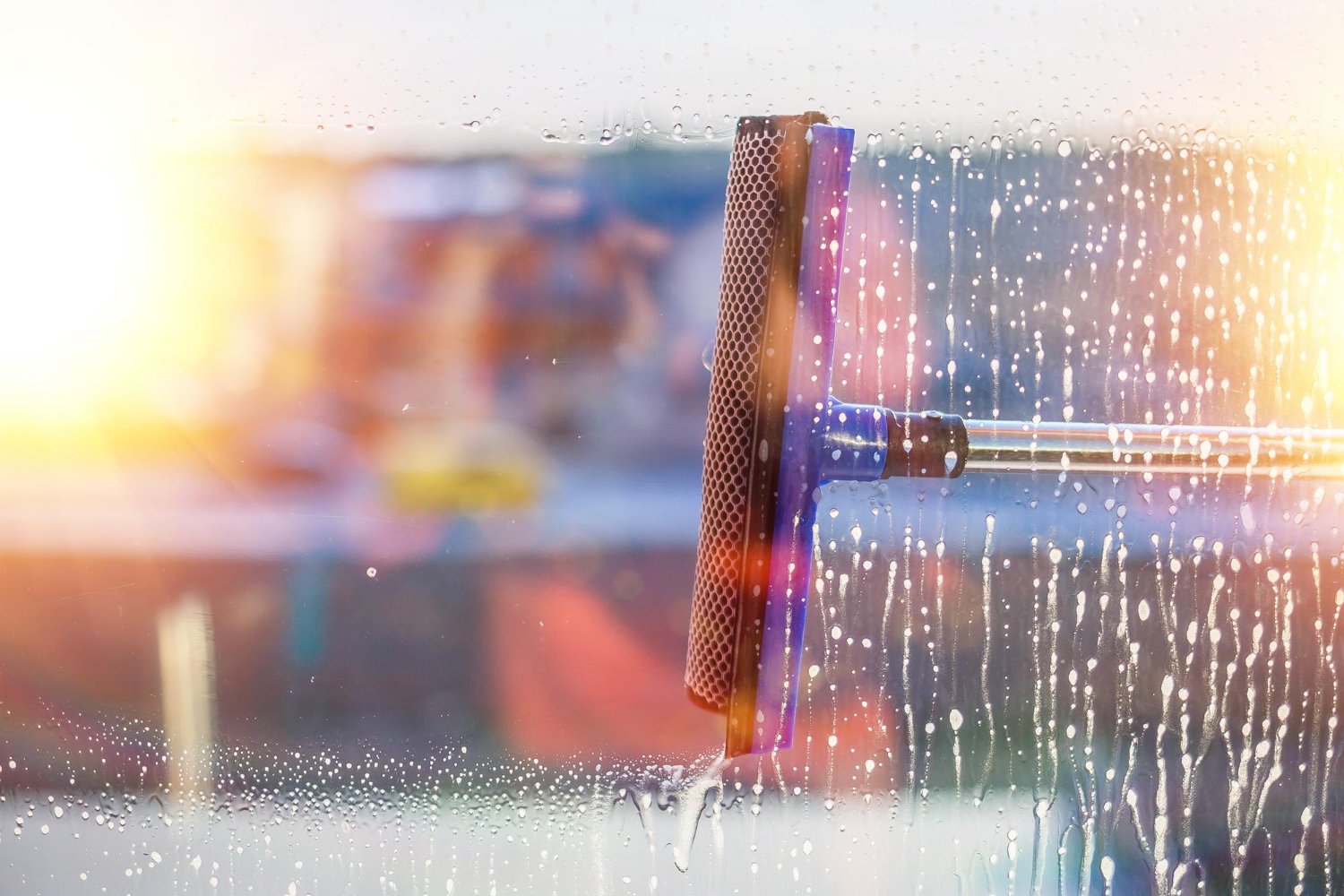 Window being cleaned with a squeegee and sponge on a rainy glass surface; blurred interior in the background.