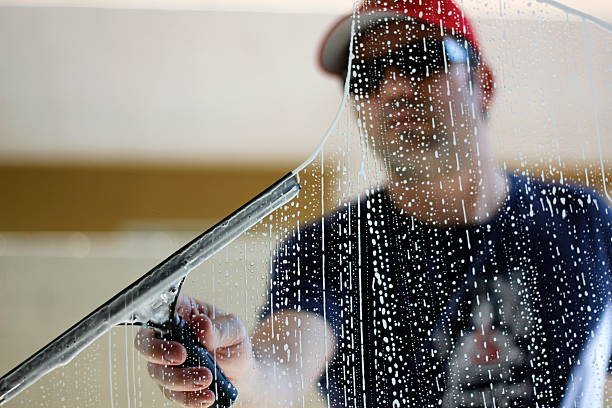 Person wearing a red cap cleaning a glass window with a squeegee, water droplets streaking the pane